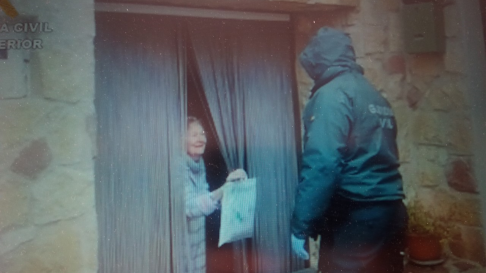 Un guardia entrega un paquete de medicinas a una pareja de mayores en un pueblo.