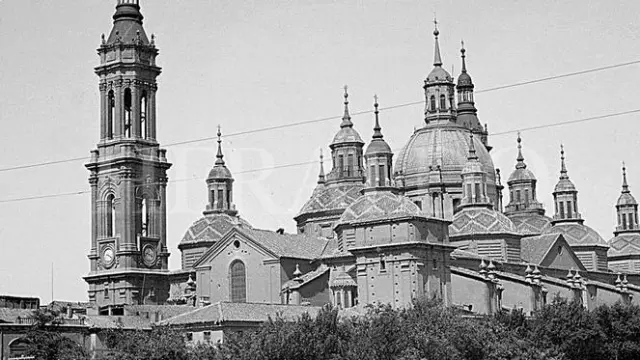 Vista del templo del Pilar de Zaragoza (fue Basílica en 1948), con solo dos torres, desde el puente de Piedra en 1929. En la fotografía, se ve como las mujeres cruzaban el puente, cargadas con sus cestas, para ir a atender sus faenas. La barandilla metálica colocada en 1908 pervivió en el puente hasta 1991