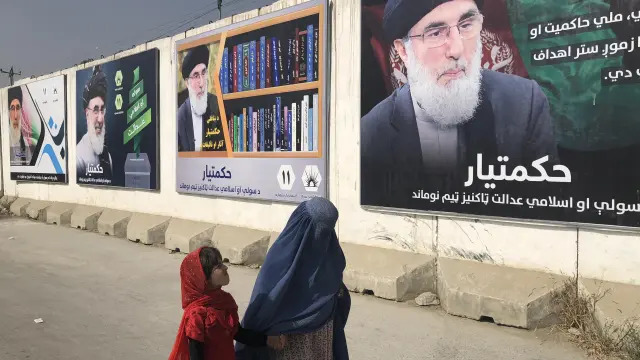Una mujer con burka y una niña pasan por un muro con publicidad electoral del señor de la guerra Gulbudin Hekmatyar