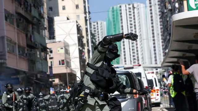 Un policía lanza una granada de gas contra manifestantes en una calle de Hong Kong.
