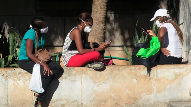 Jóvenes con mascarillas miran sus móviles en una calle de La Habana.
