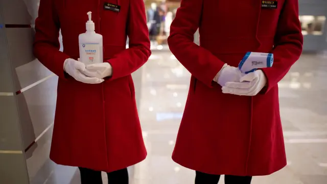 Dos empleadas de un centro comercial de Wuhan esperan a clientes con gel desinfectante y un termómetro.