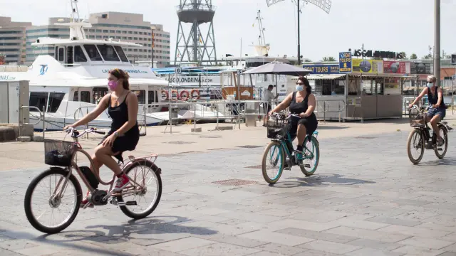 Tres turistas pasean por el puerto de Barcelona con bicicleta.