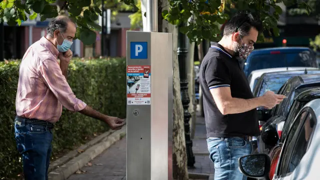 Un usuario paga en el parquímetro en la zona azul de Zaragoza, mientras otro utiliza el teléfono móvil.
