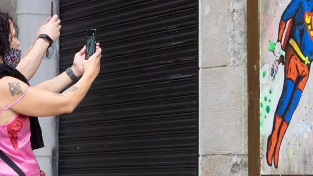 Dos personas fotografían un grafitti en una pared de Barcelona que representa a Trump vestido de Superman.