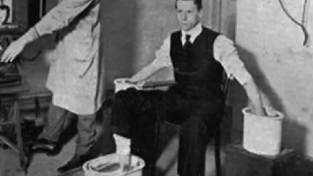 Willem Einthoven prueba el galvanómetro de hilo con un paciente, con manos y pies desnudos dentro de cubetas de disolución salina (1916)