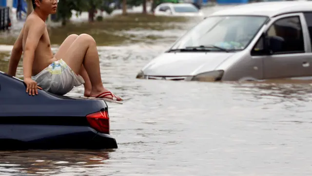 Un joven subido a un coche en una carretera inundada tras las fuertes lluvias en Zhengzhou.
