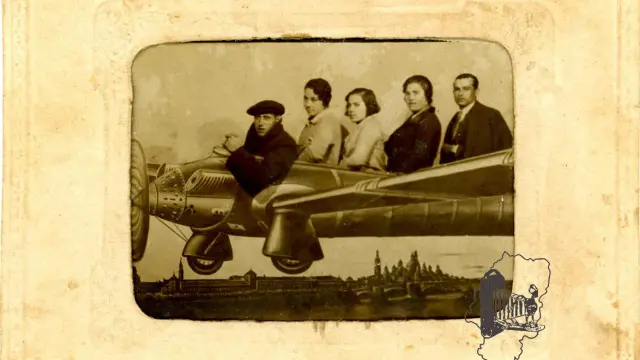 Tres mujeres y dos hombres dentro de un aeroplano pintado en un telón con vista de Zaragoza