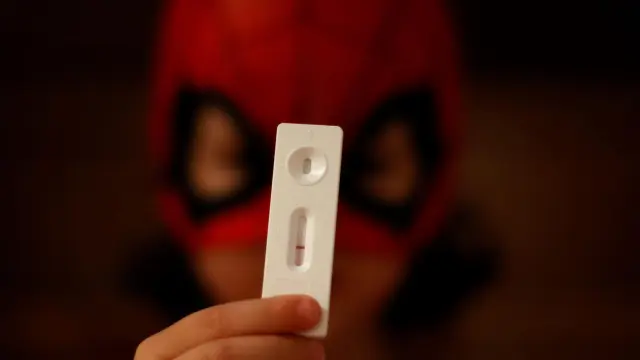 Un niño vestido de Spiderman muestra el resultado de un test de antígenos.