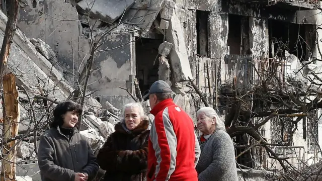 Local residents speak in front of a damaged block of flats in Mariupol