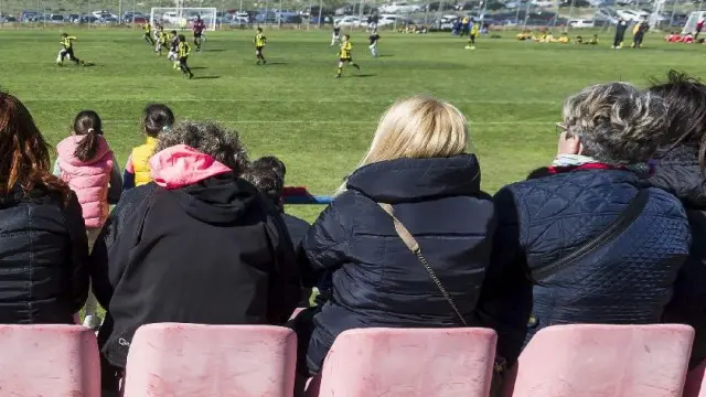 Un partido del fútbol base del Real Zaragoza en la Ciudad Deportiva, observado por padres y madres en las gradas.