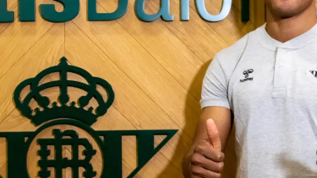 Kevin Carlos, ya en Sevilla, posa junto al escudo del Betis.