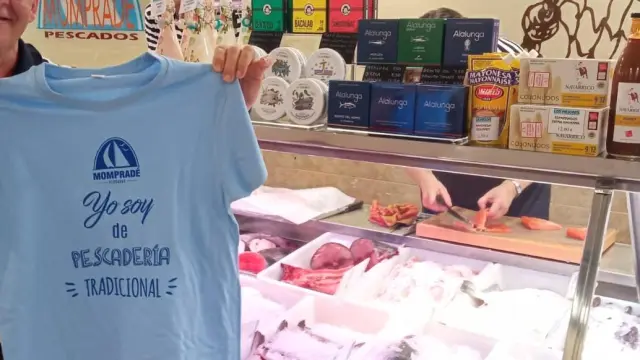 Fernando Mompradré, en la pescadería que lleva su nombre en Huesca, posa con la camiseta que repartirá entre sus clientes para reivindicar la supervivencia de este tipo de comercios especializados.