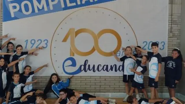 Algunos alumnos del colegio Pompiliano de Zaragoza, junto al cartel del centenario, en el pabellón deportivo del centro.