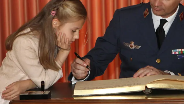 Leonor de Borbón mira como su padre don Felipe firma un libro durante la entrega de despachos de Teniente a la XLI promoción de la Academia General del Aire en Murcia, el 2 de mayo de 2014. Gran parte del aprendizaje de la Princesa de Asturias se ha producido con el ejemplo de su padre.