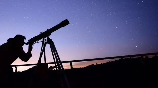 Unos visitantes del Monasterio de El Olivar observan el cielo estrellado con un telescopio avanzado.