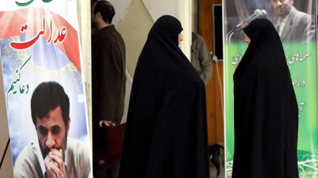 Dos mujeres caminan entre carteles con la foto del presidente iraní