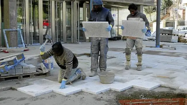 Albañiles inmigrantes trabajando en una calle, colocando baldosas