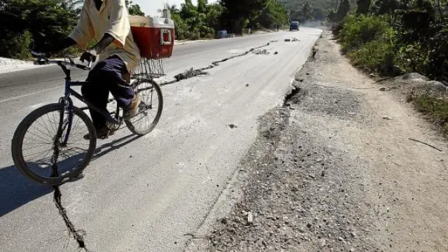 Un hombre pasa en bicicleta por una carretera agrietada a las afueras de Leogane, el viernes