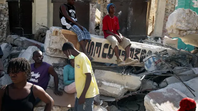 Varios ciudadanos haitianos junto a los escombros de un edificio derruído por el terremoto