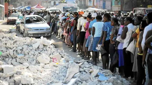 Los haitianos hacen fila para recibir alimentos junto a unos escombros, ayer en Puerto Príncipe