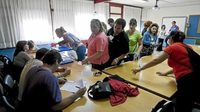 Varios padres y madres hacen fila para votar en la sala de reuniones del colegio.