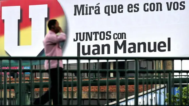 Un hombre habla por el móvil mientras camina frente a una valla publicitaria del candidato Juan Manuel Santos, ayer en Cali.