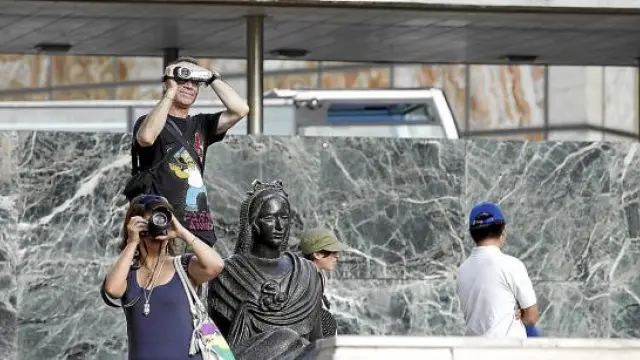 Dos turistas, cámara en mano, inmortalizan la plaza del Pilar de Zaragoza.