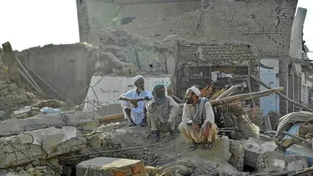 Tres hombres paquistaníes descansan entre las ruinas cercanas al lugar del atentado.