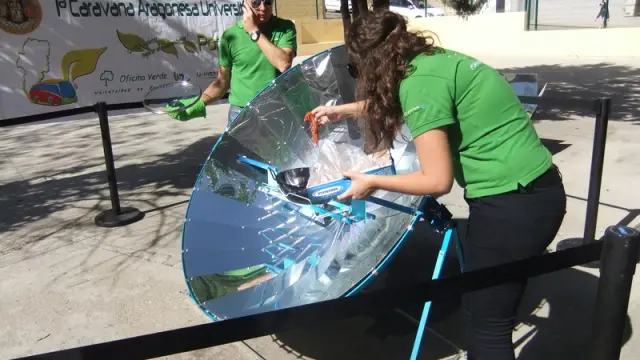 Una voluntaria acerca un langostino a la olla que recibe los rayos solares de la parabólica.