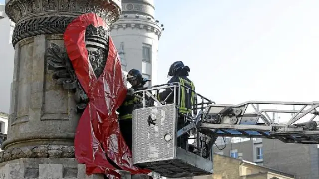 Los Bomberos colocan un gran lazo rojo en el monumento de la plaza de España.