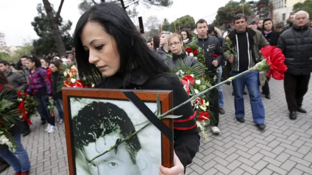 Una manifestante porta un retrato de un fallecido y un clavel