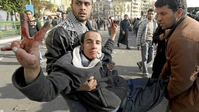 Dos egipcios trasladan a un herido durante los enfrentamientos en la plaza de Tahrir, ayer en El Cairo.