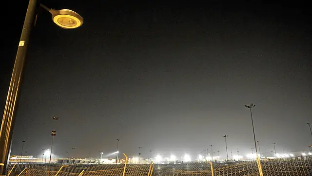 En primer plano, una de las farolas apagadas del parquin norte de la Expo. Al fondo, iluminados, los campos de entrenamiento de la Federación de Atletismo