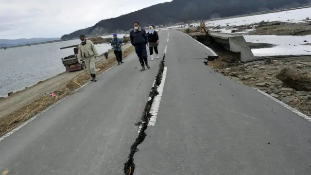 Un grupo de personas caminan por una carretera afectada por el terremoto y posterior tsunami