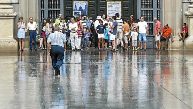Paseantes y turistas se refugian de una tormenta en la entrada a la basílica del Pilar.