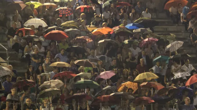 Los asistentes al concierto resguardados bajo los paraguas