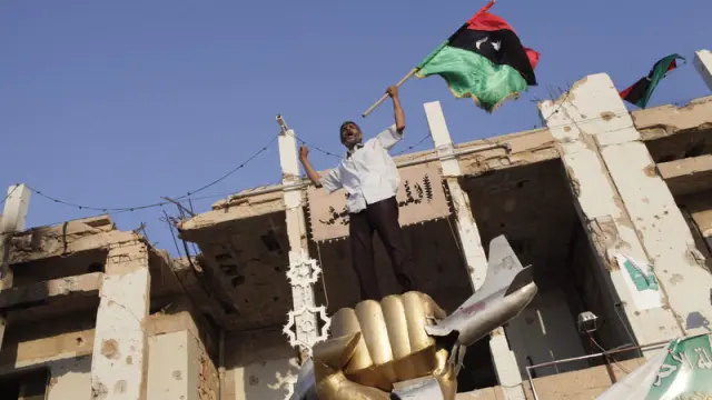Un rebelde libio ondea su bandera sobre el monumento símbolo del dictador libio