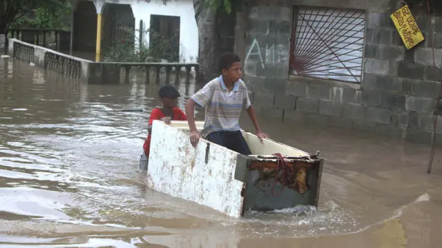 Un joven transportando a otro en medio de una calle inundada