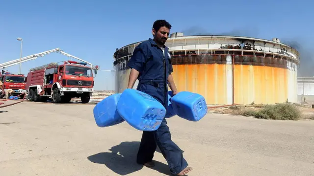 Un hombre carga botes vacíos junto a un tanque de petróleo en Brega