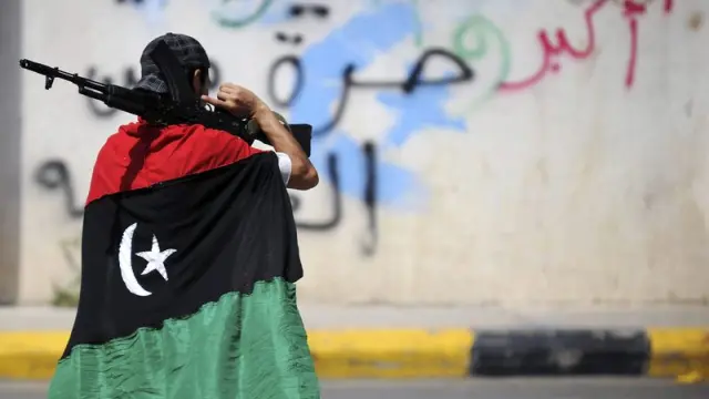 Un rebelde se cubre con una bandera de Libia