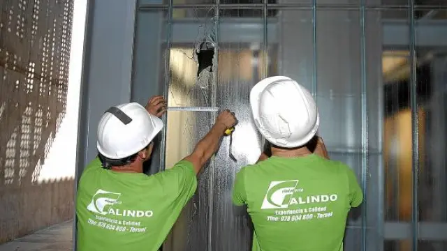 Dos operarios toman medidas para reponer el cristal de la caja del ascensor roto de un botellazo.