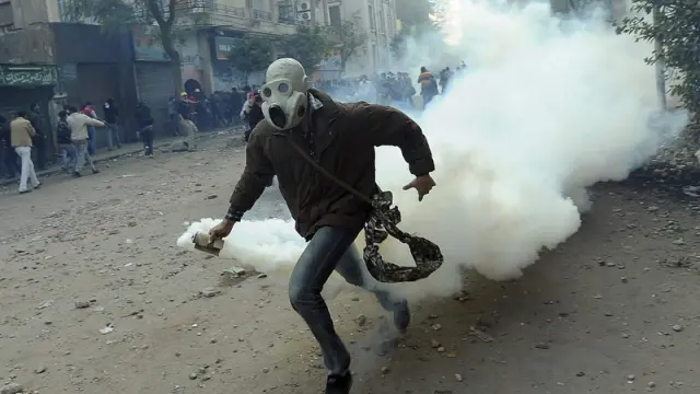 Un manifestante retira una botella de gas lacrimógeno lanzada por la policía