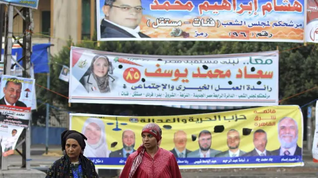 Dos mujeres y un niño pasean ante carteles electorales en El Cairo