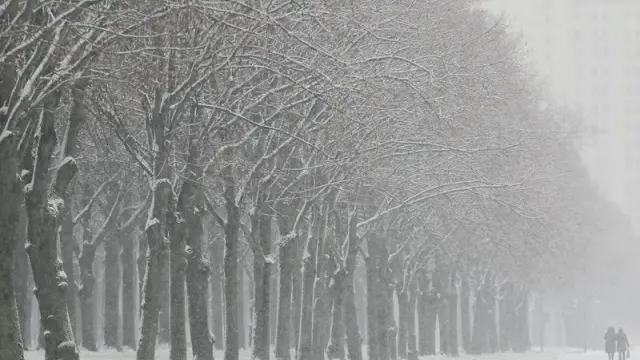 Dos personas pasean por una avenida cubierta de nieve frente a la Universidad de Moscú.