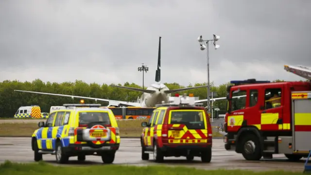 Coches de la policía británica y los bomberos permanecen aparcados junto al avión