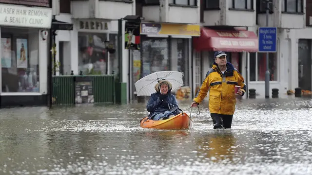 Un hombre remolca a una mujer a bordo de una piragua en una calle inundada en Datchet.