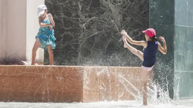 Dos niñas juegan en una fuente de Zaragoza en verano