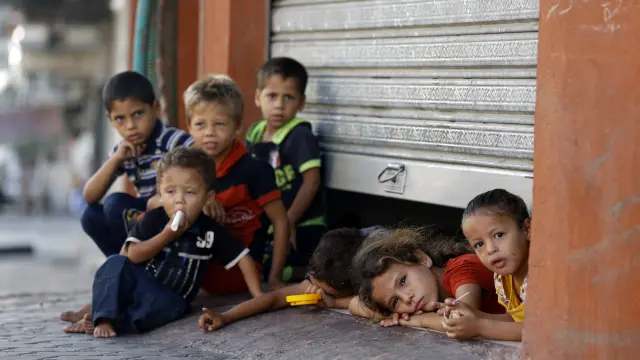 Niños palestinos se asoman a la calle desde el refugio que comparten con sus familias