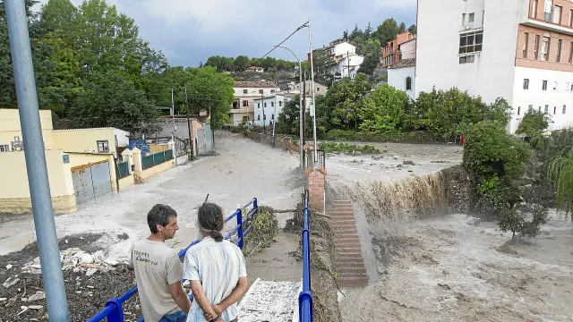 Dos vecinos observan el desbordamiento del barranco del Jorgito que forma una cascada mientras, a la izquierda, el agua se remansa al taponarse el desagüe hacia el Turia.